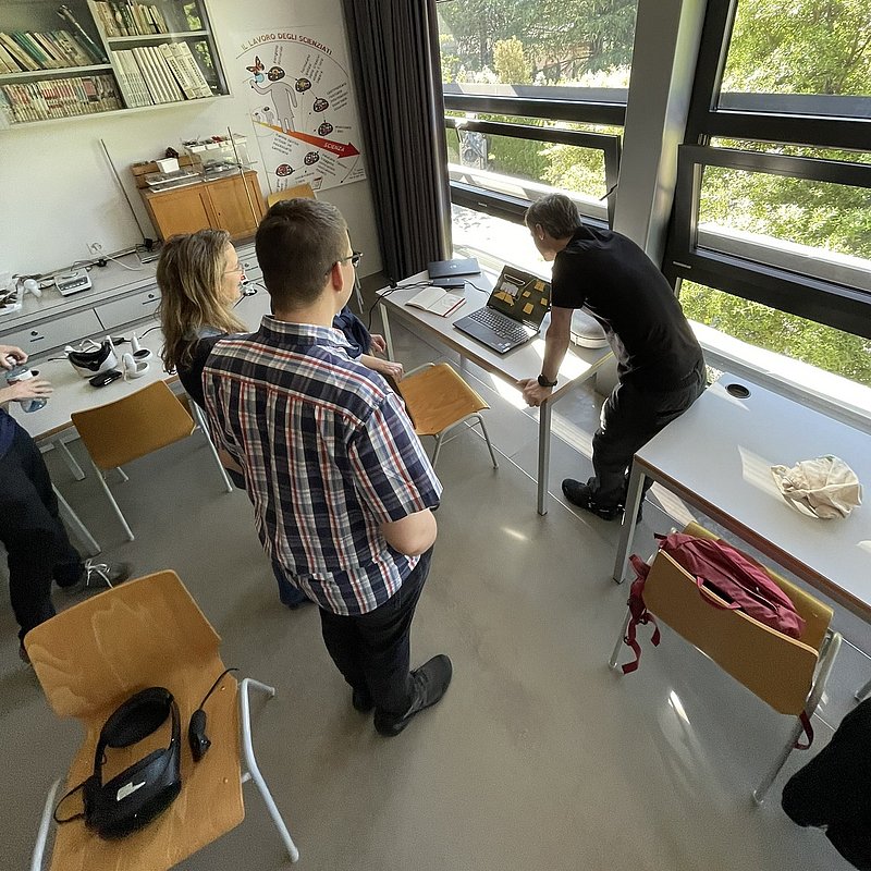 Kolleginnen und Kollegen des Dozenten verfolgen seinen Unterricht auf dem Laptop.